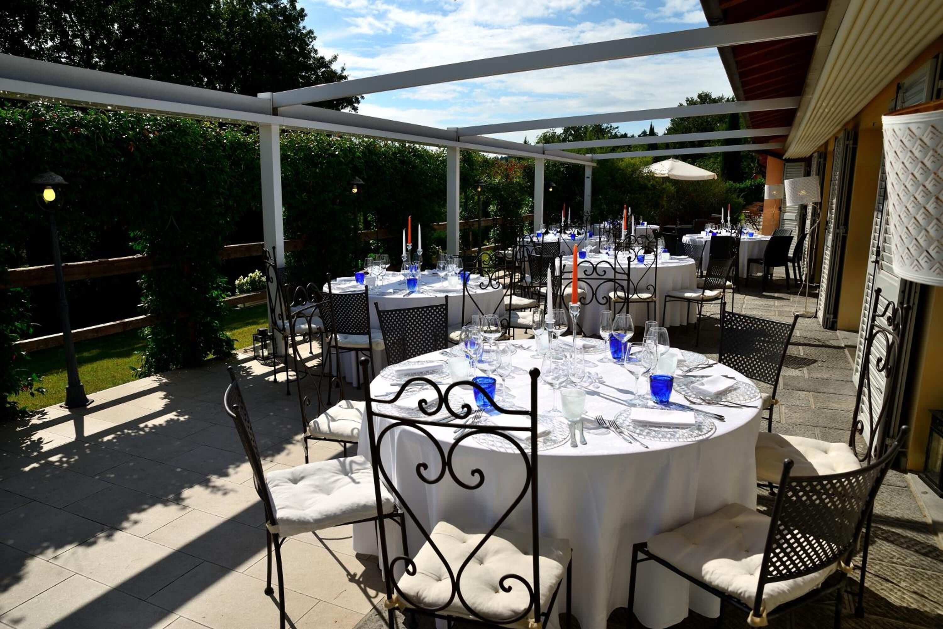 Eine Terrasse im Freien mit runden Tischen, die zum Essen gedeckt sind, umgeben von Stühlen und Sonnenschirmen.