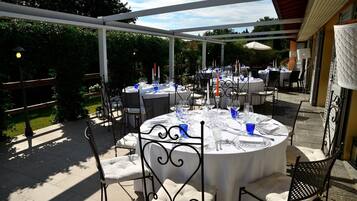 Eine Terrasse im Freien mit runden Tischen, die zum Essen gedeckt sind, umgeben von Stühlen und Sonnenschirmen.