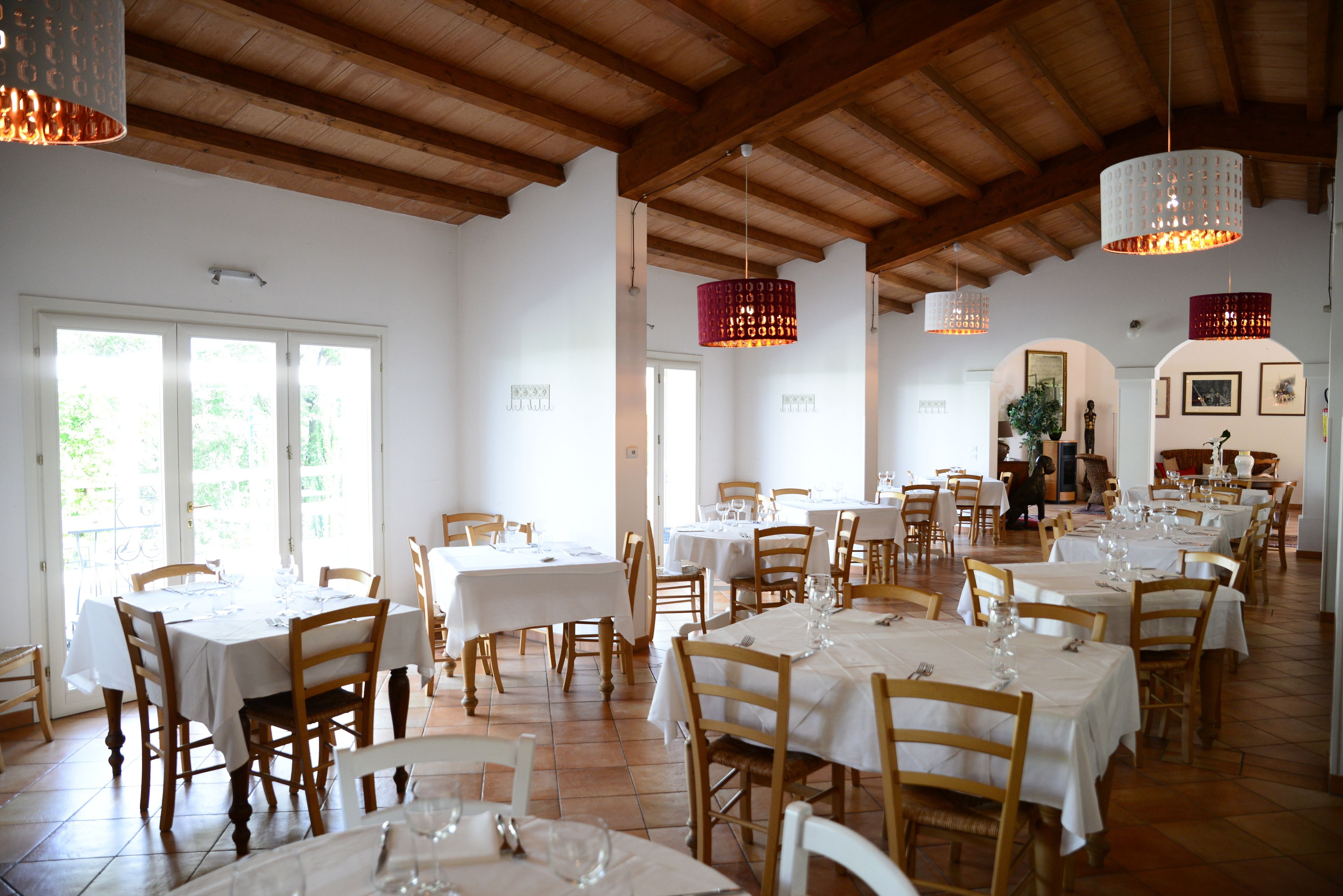 Ein Restaurant mit mehreren Esstischen, Holzsesseln und hängenden Pendelleuchten.