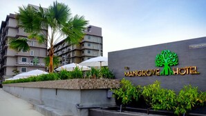 The Mangrove Hotel sign with a tree logo, surrounded by palm trees and outdoor umbrellas.