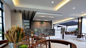 A modern hotel lobby with a reception desk, wooden chairs, and a dining area.