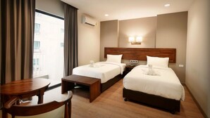 A hotel room with two single beds, a wooden desk, a chair, a nightstand, and a window with curtains.