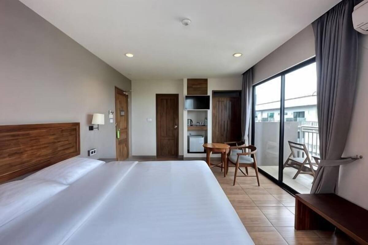 A hotel room with a large bed, a desk, a chair, a balcony with a view, and a kitchenette.