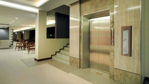 A modern hotel lobby with a marble wall, an elevator, and a staircase leading to another floor.