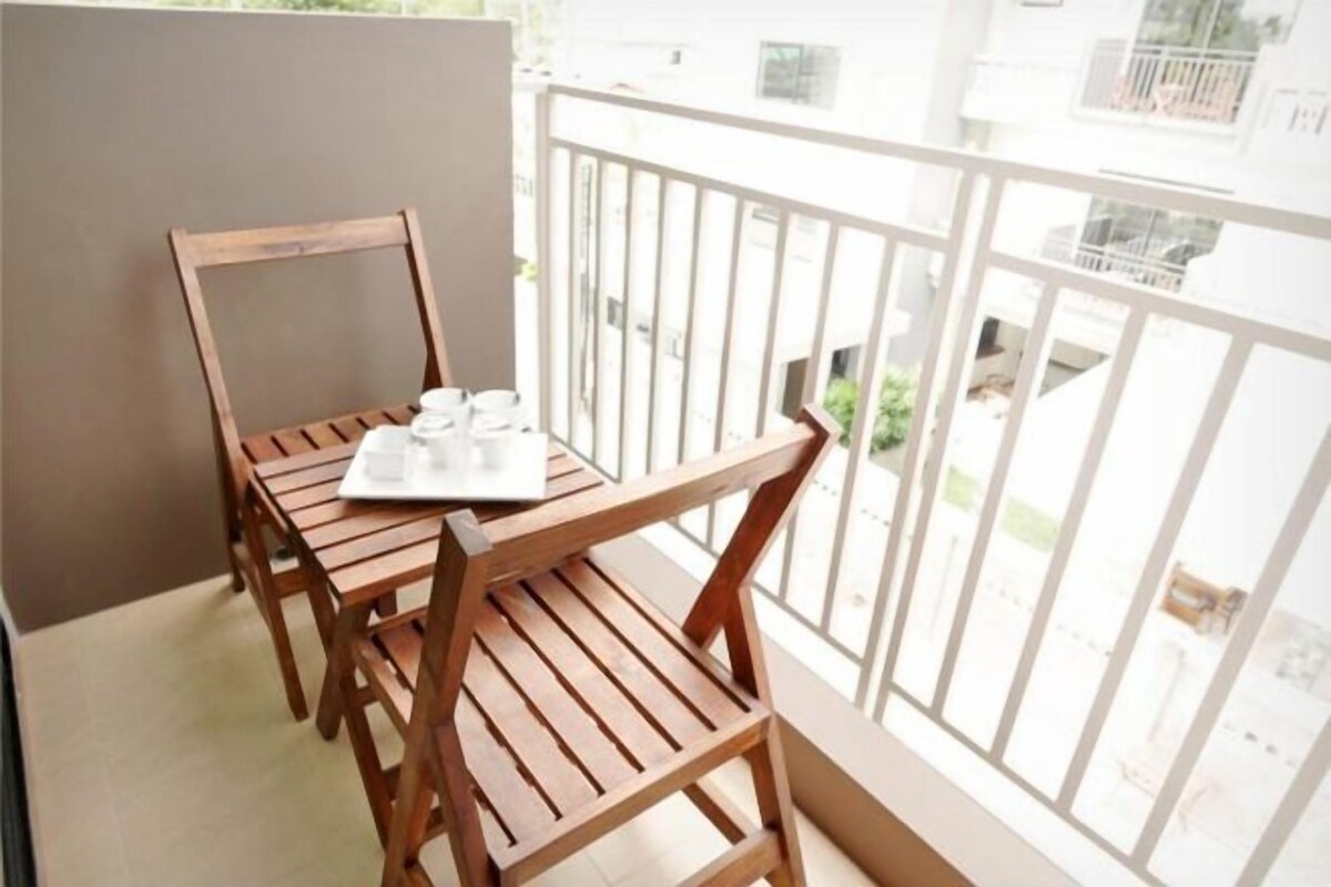 A balcony with a wooden table and chairs, a white railing, and a view of a residential area.