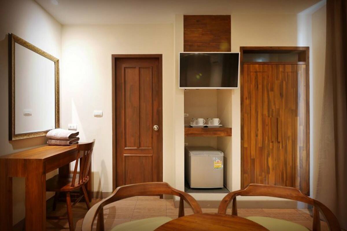 A compact room with a wooden desk, two chairs, a small refrigerator, and a television mounted on the wall.