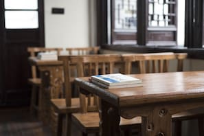 A wooden table with a book on it, surrounded by wooden chairs in a room with windows.