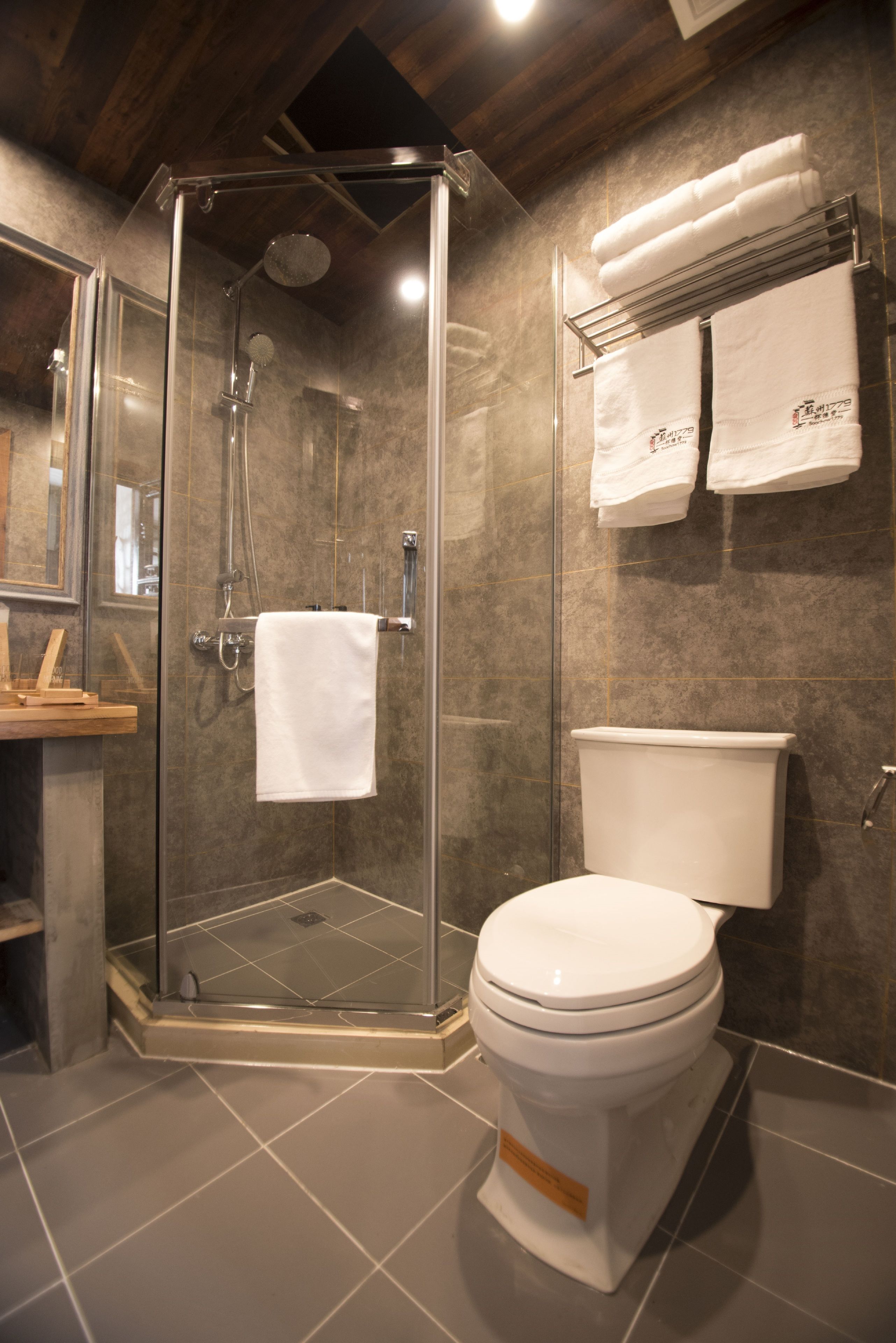 A modern bathroom with a glass-enclosed shower, a white toilet, and a towel rack with folded towels.