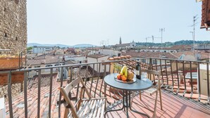 A balcony with a table set with fruit and a bottle, overlooking a cityscape with terracotta rooftops and buildings. - 1200 Torre Donati Apartments by Mmega (Florence)