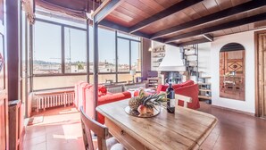 A spacious living area with a wooden table, red sofas, and large windows offering a view of the cityscape. - 1200 Torre Donati Apartments by Mmega (Florence)