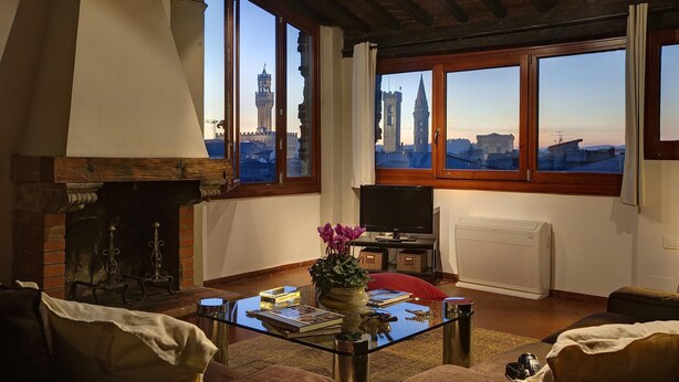 A living room with a fireplace, a television, and a large window with a city view. - 1200 Torre Donati Apartments by Mmega (Florence)