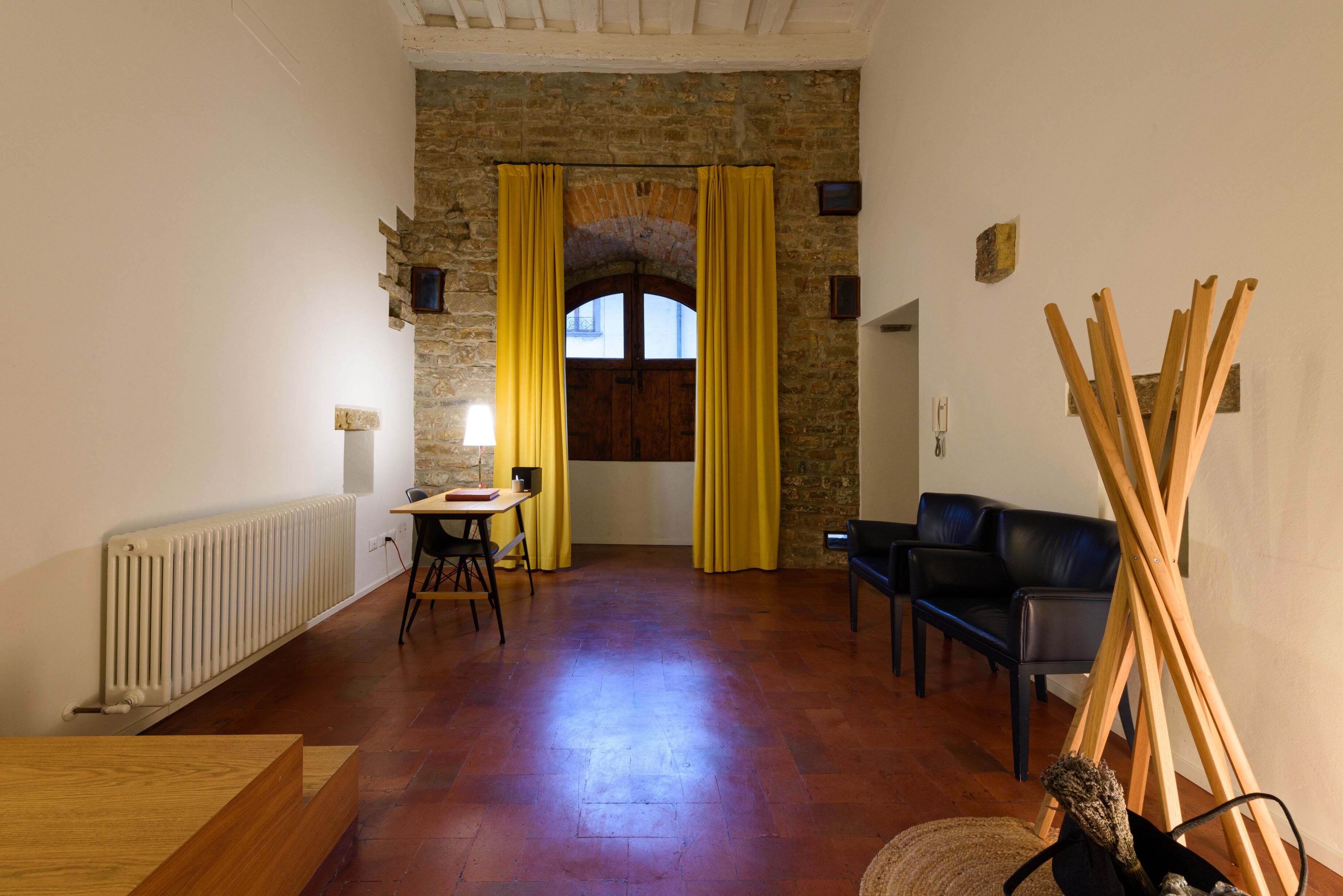 Una habitación con pared de piedra, una mesa de madera, un sillón de cuero negro y una cortina amarilla.