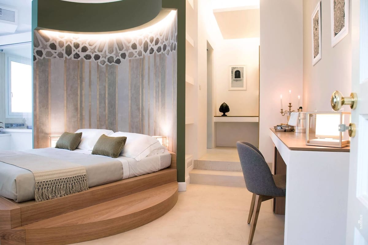 A modern bedroom with a curved bed, a desk with a lamp, and a chair.