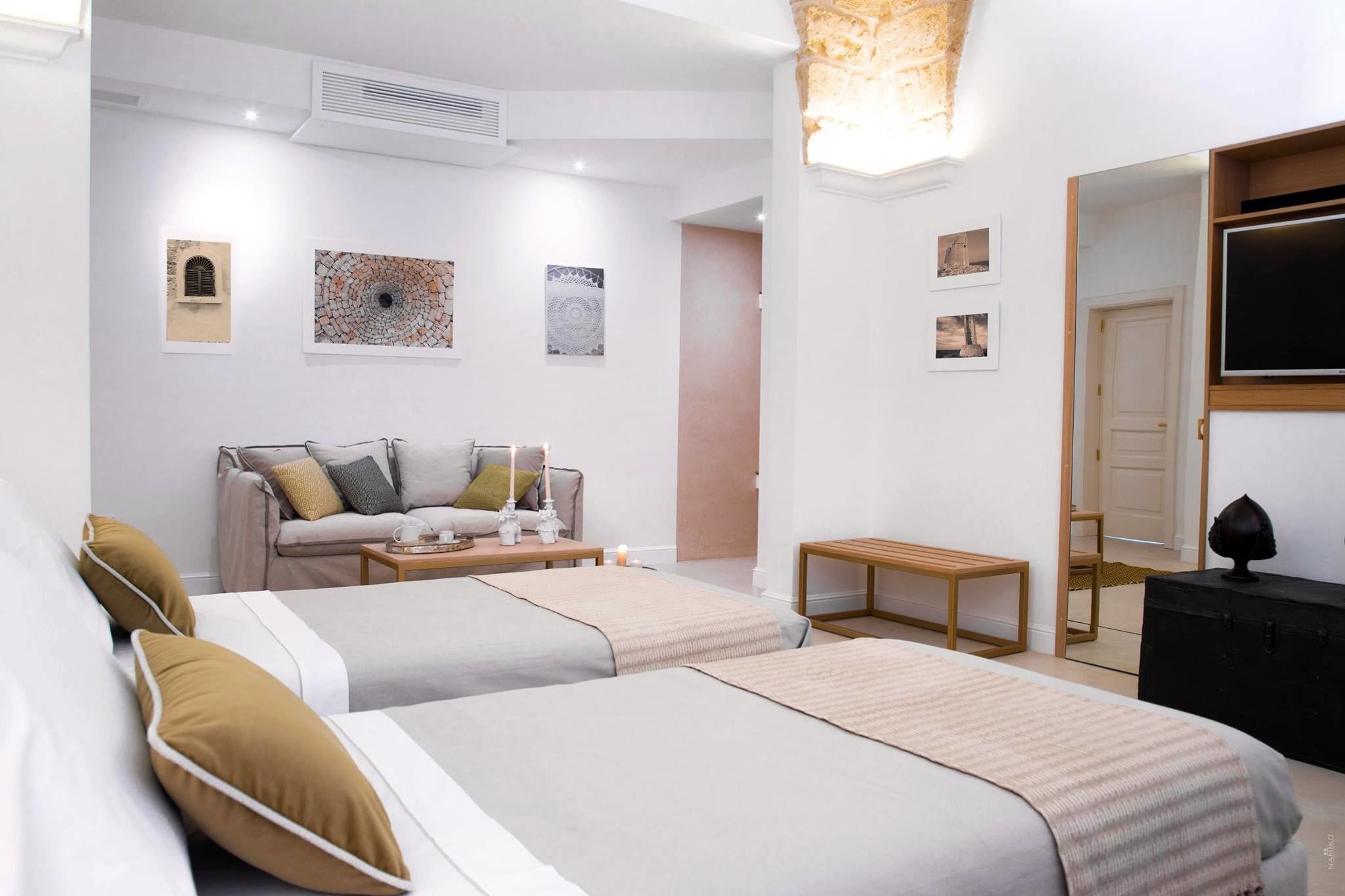 Une chambre moderne avec deux lits, un canapé, une télévision et des œuvres d’art accrochées aux murs.