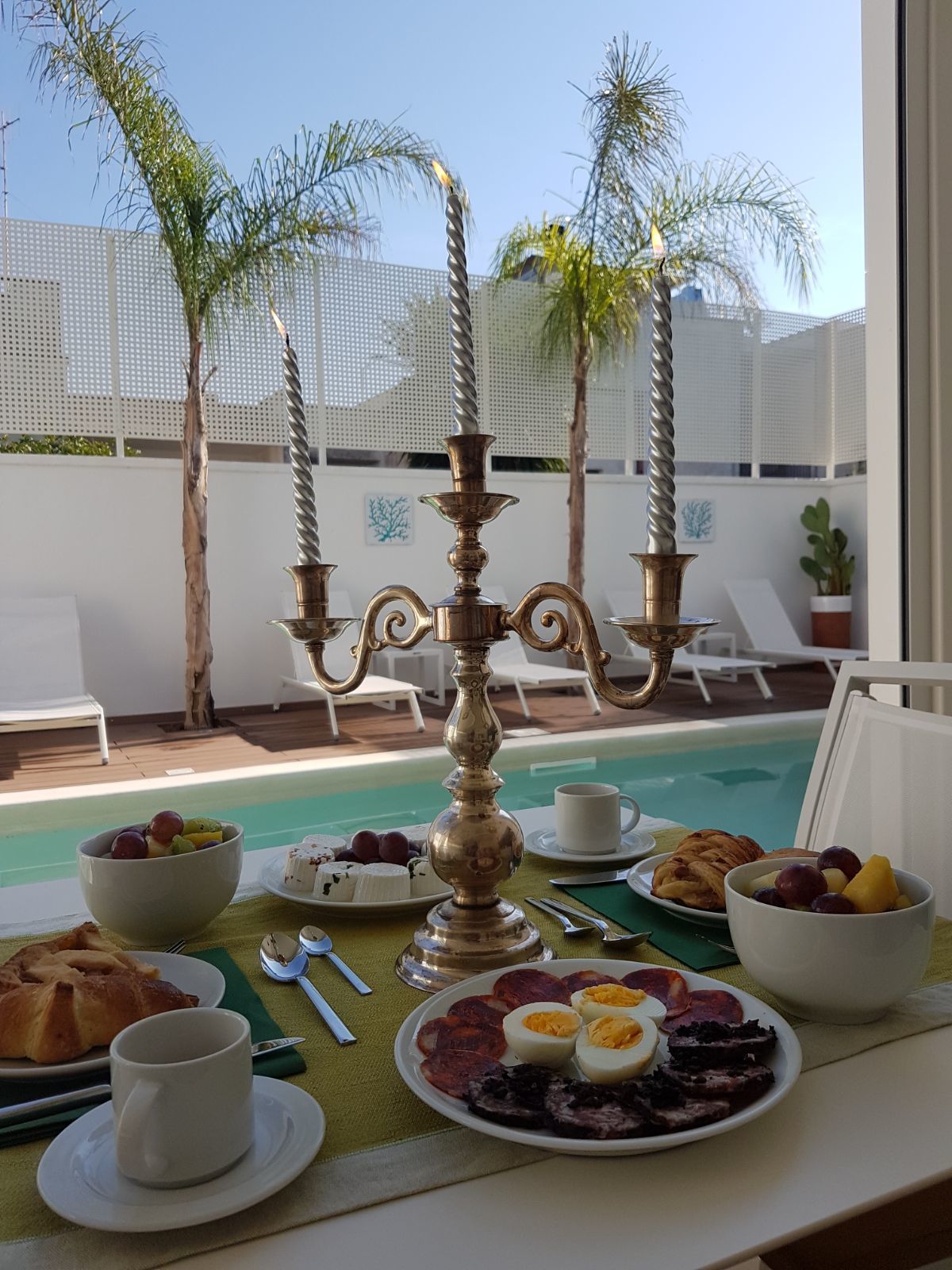 A breakfast setting with a pool view, featuring a candelabra, plates of food, and a cup.