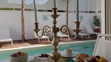 A breakfast setting with a pool view, featuring a candelabra, plates of food, and a cup.