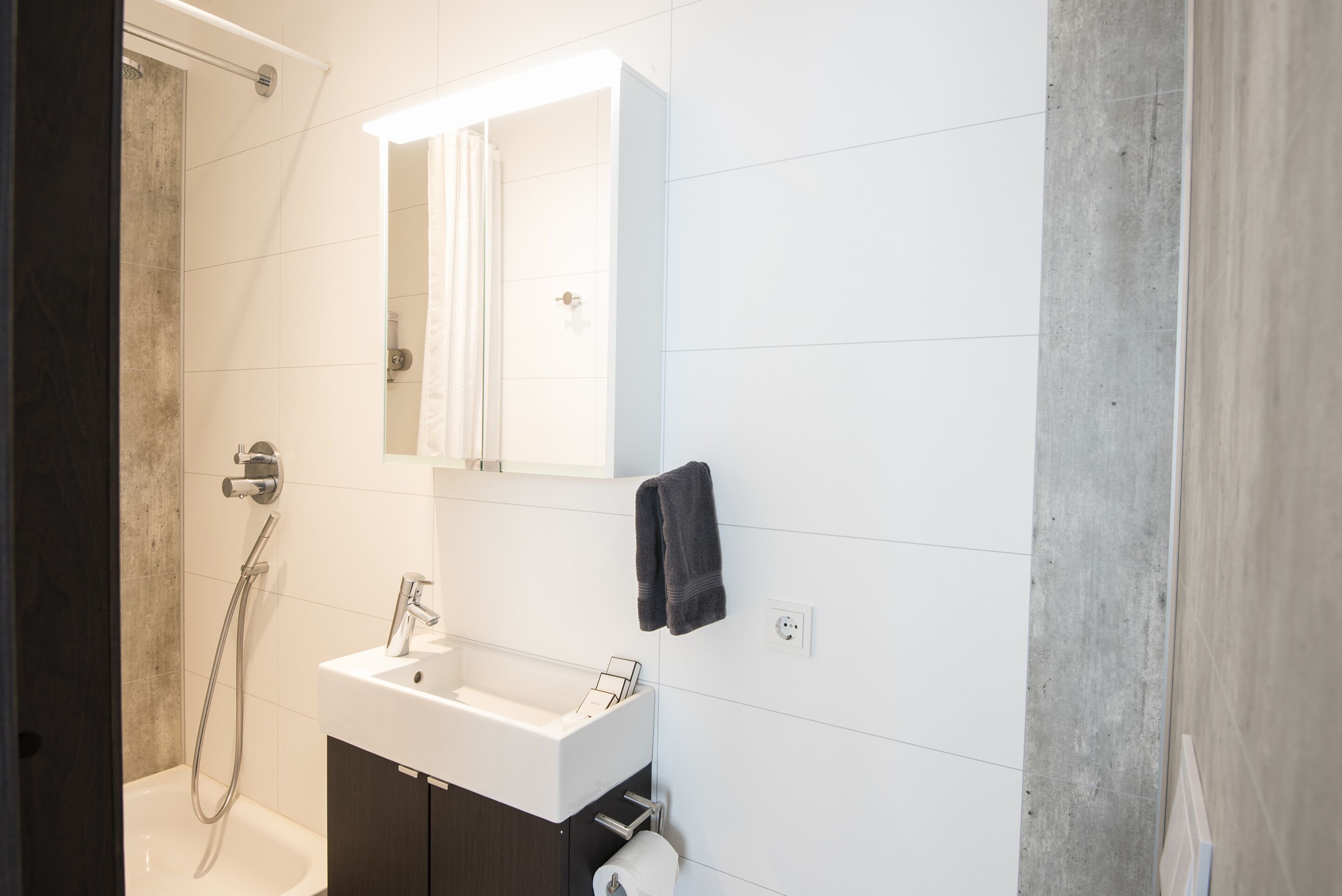 A modern bathroom with a white sink, a mirror, and a shower.