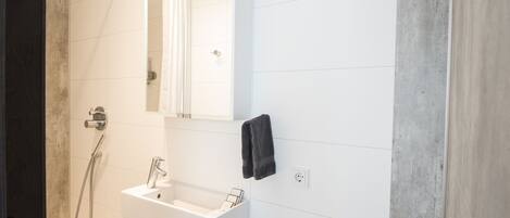 A modern bathroom with a white sink, a mirror, and a shower.