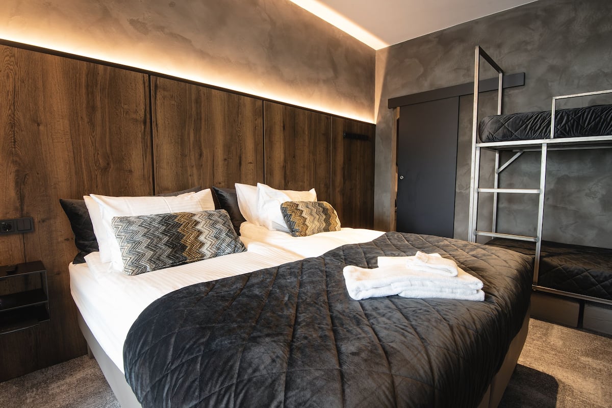 A modern bedroom with a large bed, a wooden headboard, and a bunk bed.