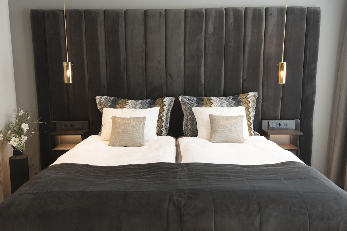 A double bed with a black headboard and two bedside tables, each with a lamp.