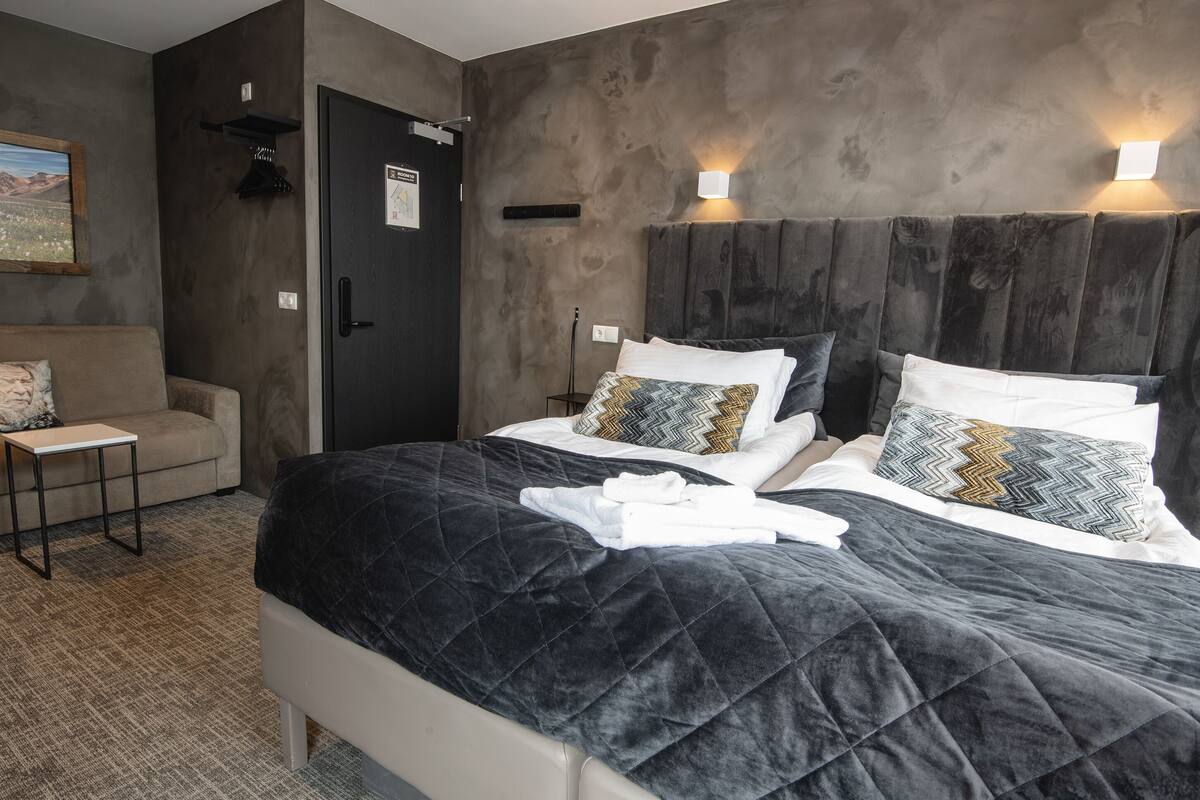 A modern hotel room with a large bed, a small table, and a sofa.