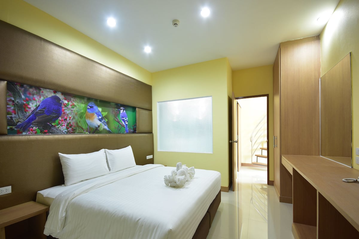 Een hotelkamer met een groot bed, een schilderij van vogels aan de muur, een raam met zonwering en een houten garderobe.