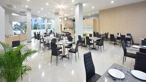 A spacious dining area with multiple tables and chairs, a central chandelier, and large windows offering a view of the outdoors. - Siam Golden Place Suvarnabhumi (Bangkok)