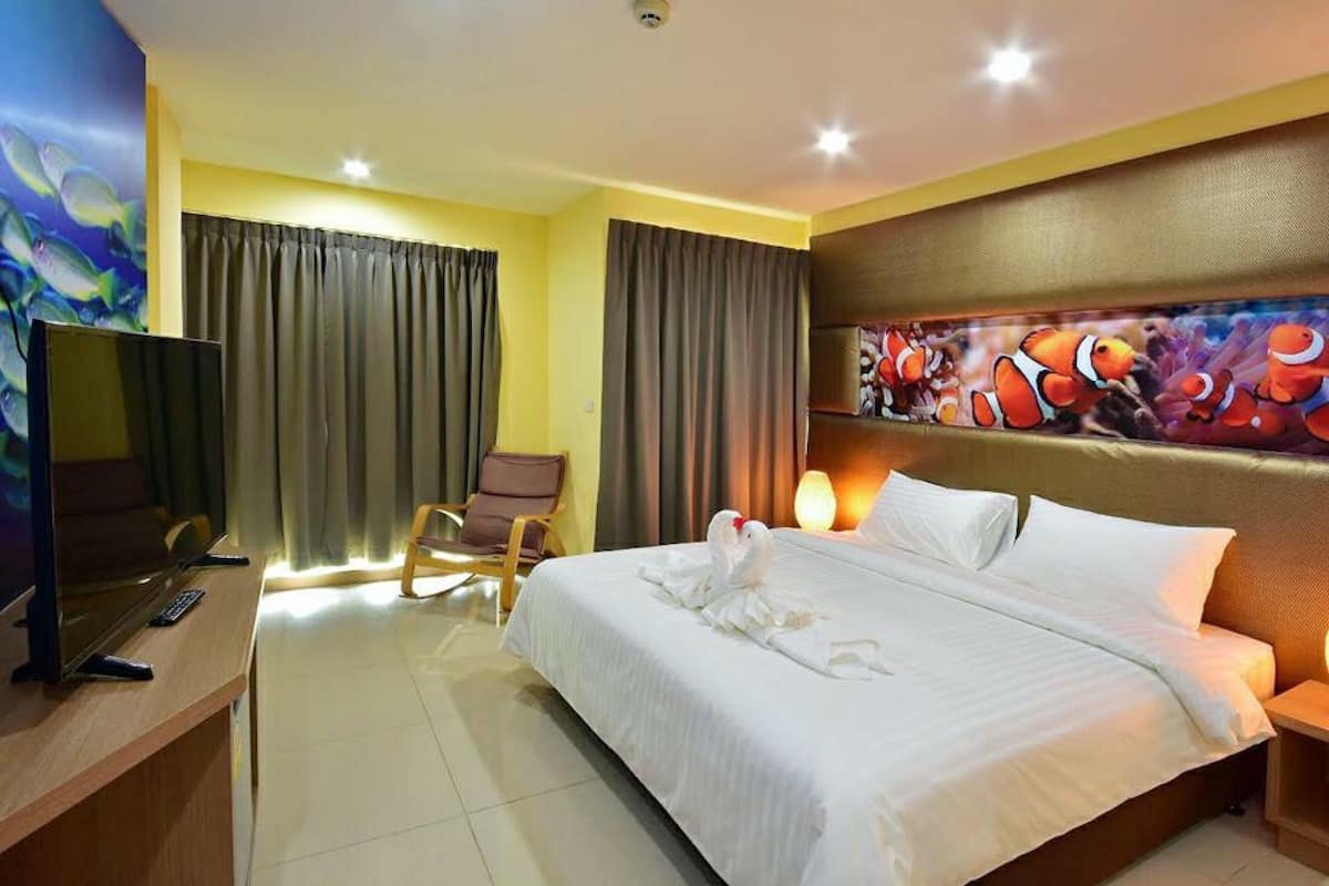 Een hotelkamer met een bed, een televisie, een stoel, gordijnen en een muur met een vis schilderij.
