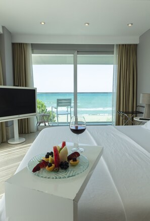 A hotel room with a bed, a TV, a dining table with fruit and wine, and a view of the ocean. - Venn Boutique Hotel - Boutique Class (Atakum)