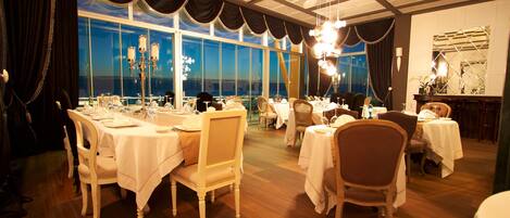 A restaurant with multiple tables set for dining, large windows, and a chandelier.