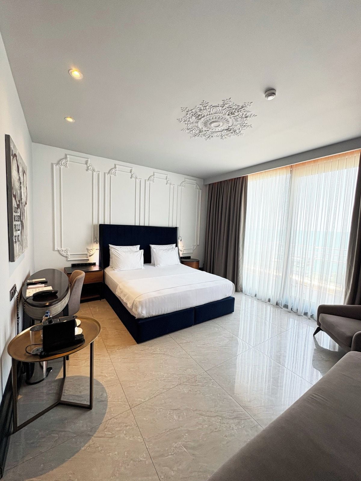 A modern hotel room with a large bed, a desk, a chair, and a sofa.