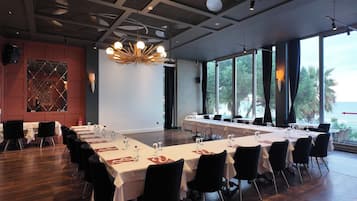 A conference room with long tables, black chairs, and a large window with a view of the sea.