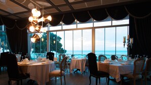 Un comedor con mesas dispuestas para el servicio, ventanas amplias con vista al mar y una araña colgando del techo.