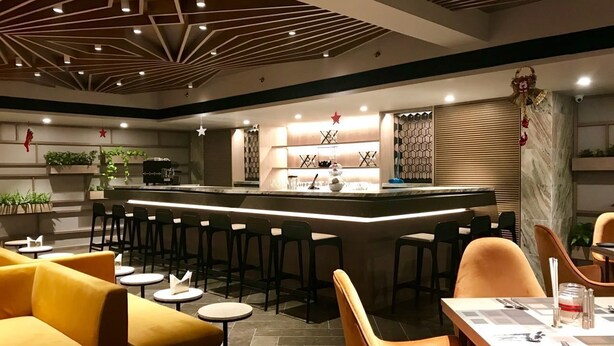 A modern bar area with a central counter, bar stools, and seating arrangements including sofas and round tables. - Levana Suites (Lucknow)