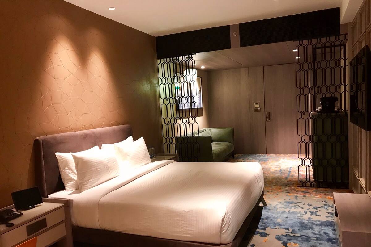 A hotel room with a large bed, a desk with a computer, a chair, and a decorative partition.