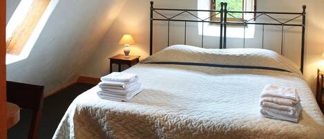 A bedroom with a bed, a nightstand, a lamp, and a window.