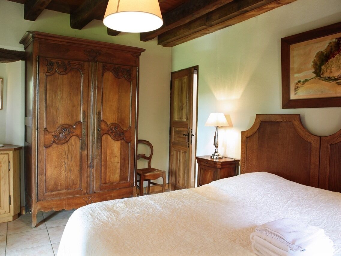Een slaapkamer met een grote houten garderobe, een bed met een witte dekbedovertrek, een houten nachtkastje en een schilderij aan de muur.