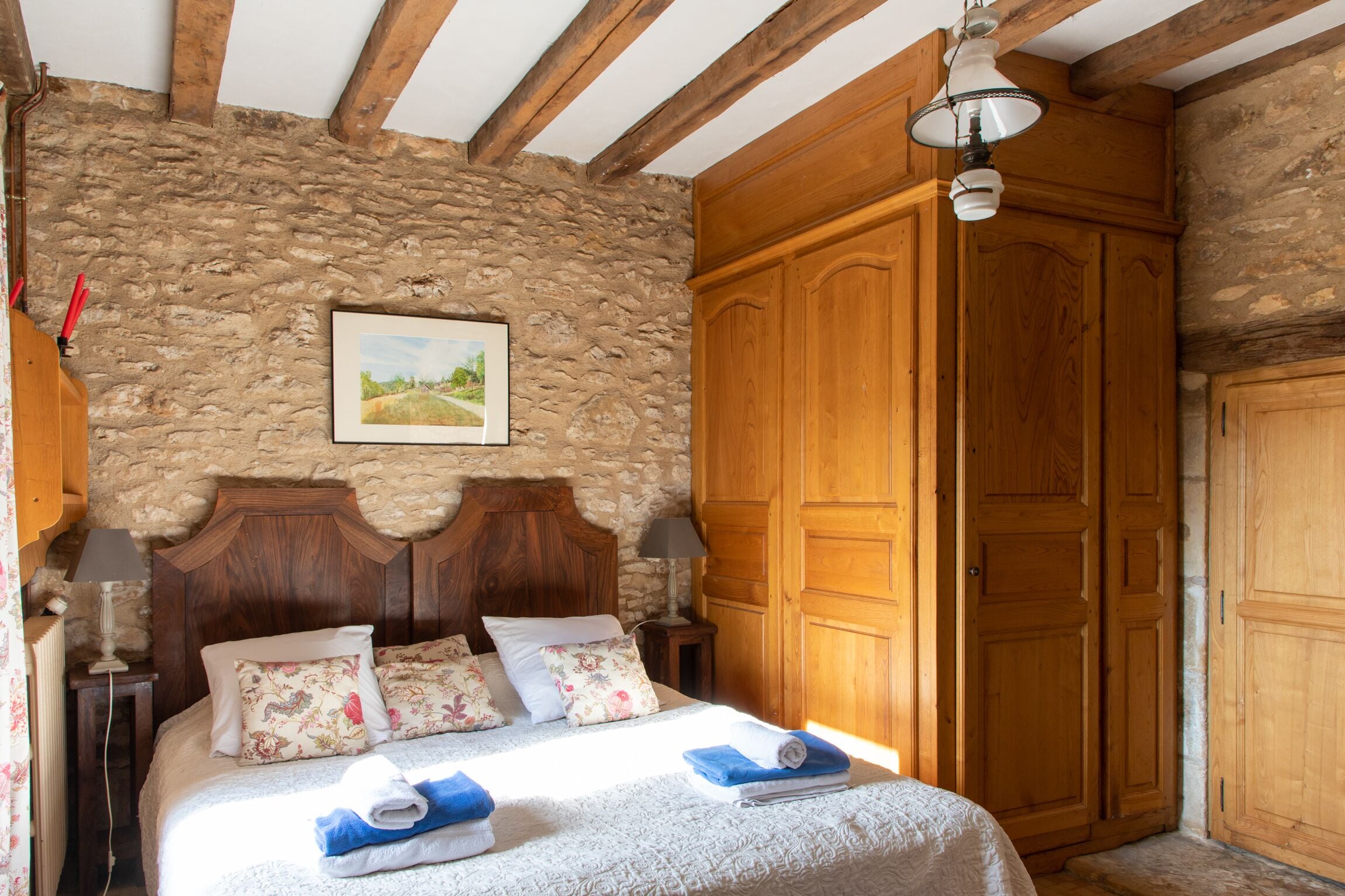 Une chambre avec un mur en pierre, un cadre de lit en bois et une grande armoire.