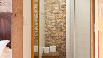 Une salle de bain avec un mur en pierre, une porte en bois, un miroir, des toilettes et une douche.