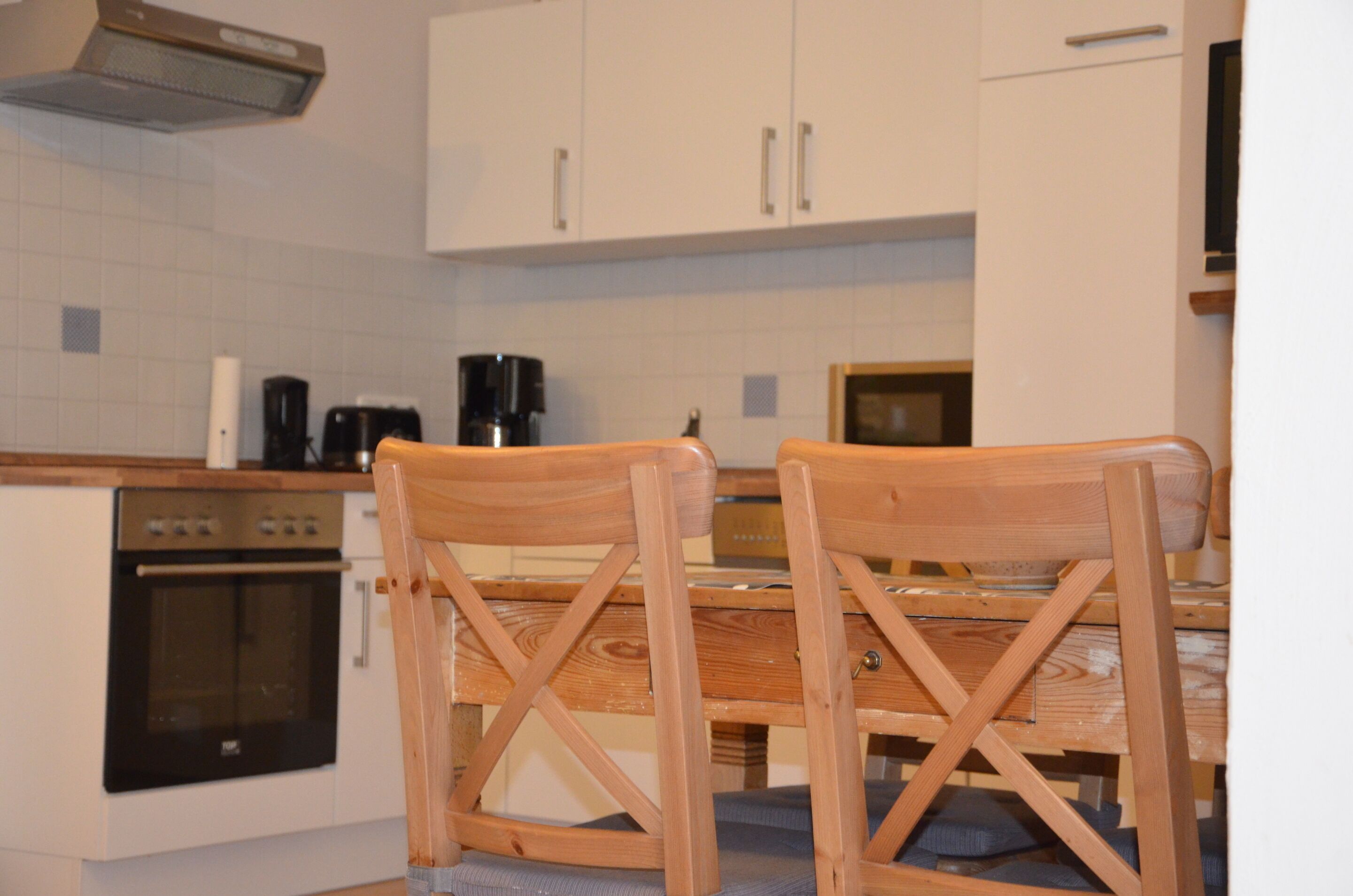 Una cocina con armarios blancos, una mesa de madera y dos sillas de madera.