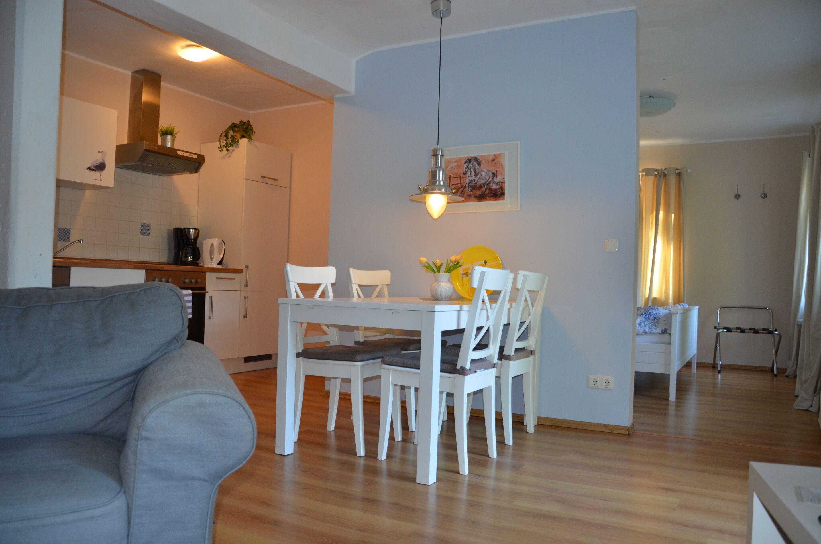 Una sala de estar moderna con un sofá gris, una mesa de comedor con sillas blancas y una zona de cocina con estufa y armarios.