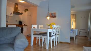 Una sala de estar moderna con un sofá gris, una mesa de comedor con sillas blancas y una zona de cocina con estufa y armarios.
