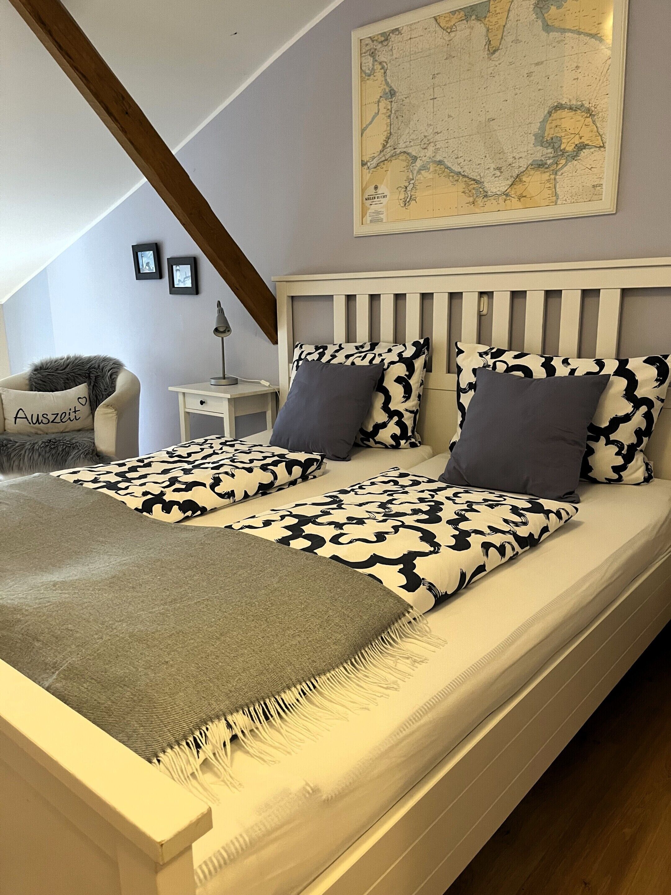 A bedroom with a bed, a map on the wall, and a chair with a cushion.