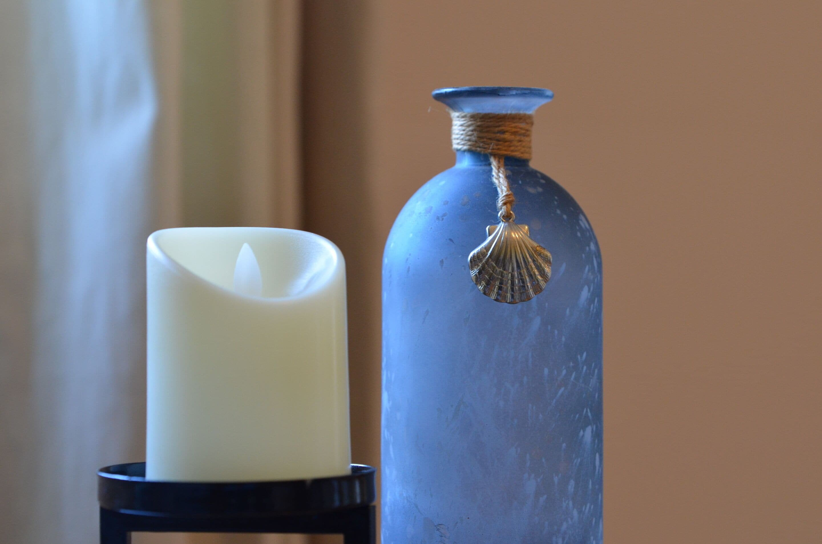 A white candle and a blue vase with a rope and shell decoration on a black stand.