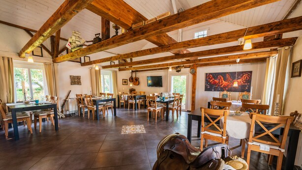 A spacious dining area with wooden tables and chairs, a large painting on the wall, and a wooden ceiling structure. - Kleines Landhotel Rehedyk (Sankt Michaelisdonn)