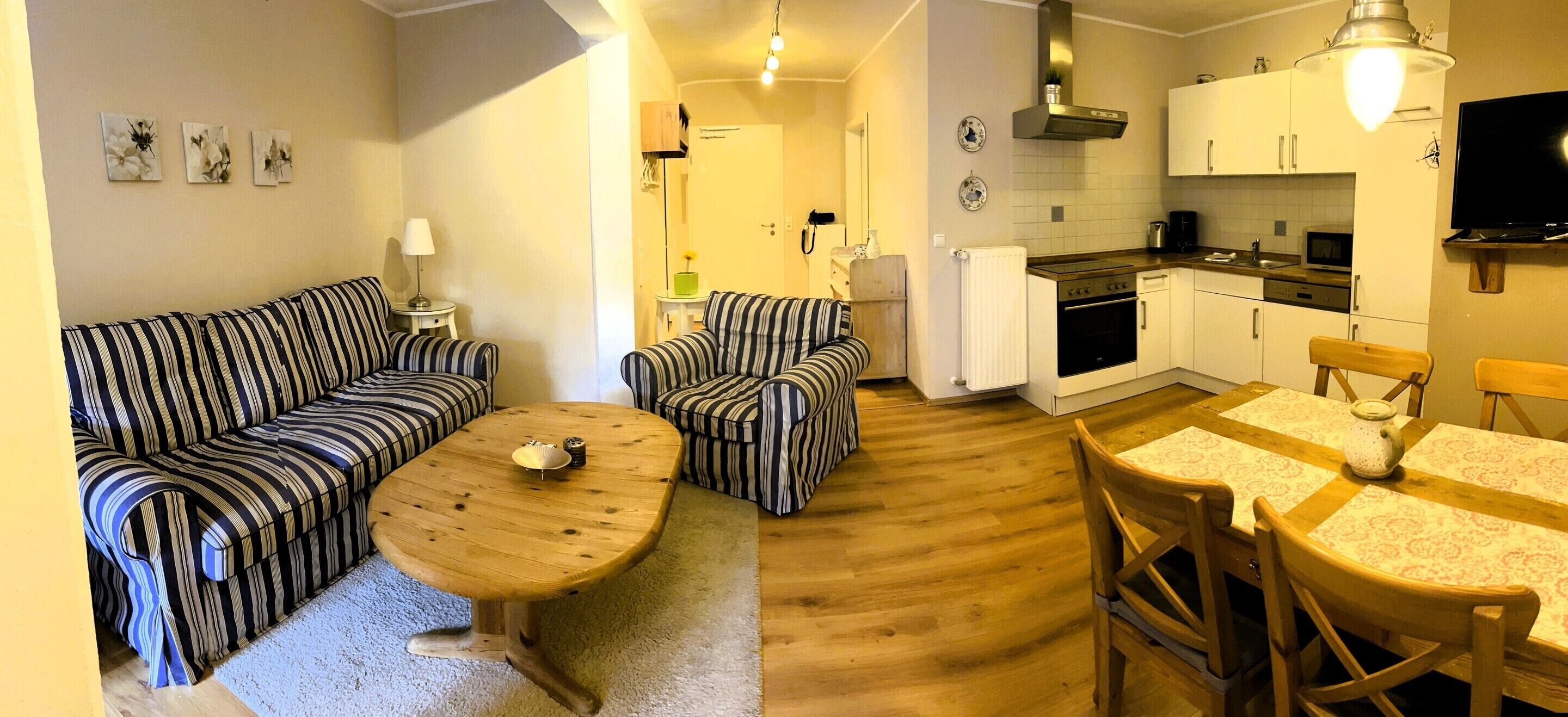 Un espacio habitable compacto con sofá, una mesa de centro de madera, una mesa de comedor con sillas, una zona de cocina con electrodomésticos y un televisor.
