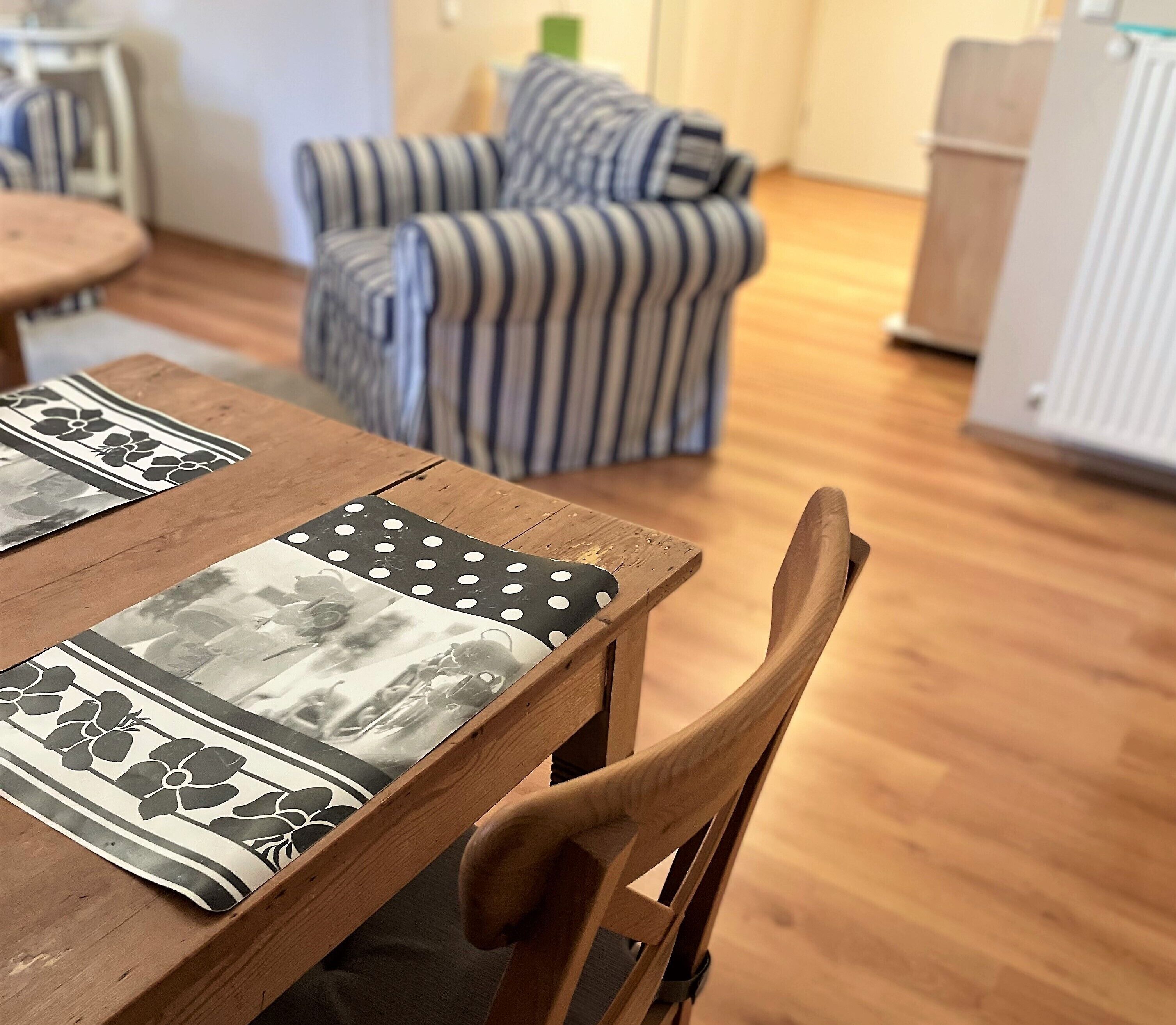 A wooden dining table with a patterned placemat, a striped armchair, and a radiator in a room with wooden flooring.