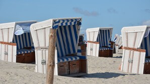 Beach chairs with striped cushions and wooden frames, arranged on a sandy beach. - Kleines Landhotel Rehedyk (Sankt Michaelisdonn)