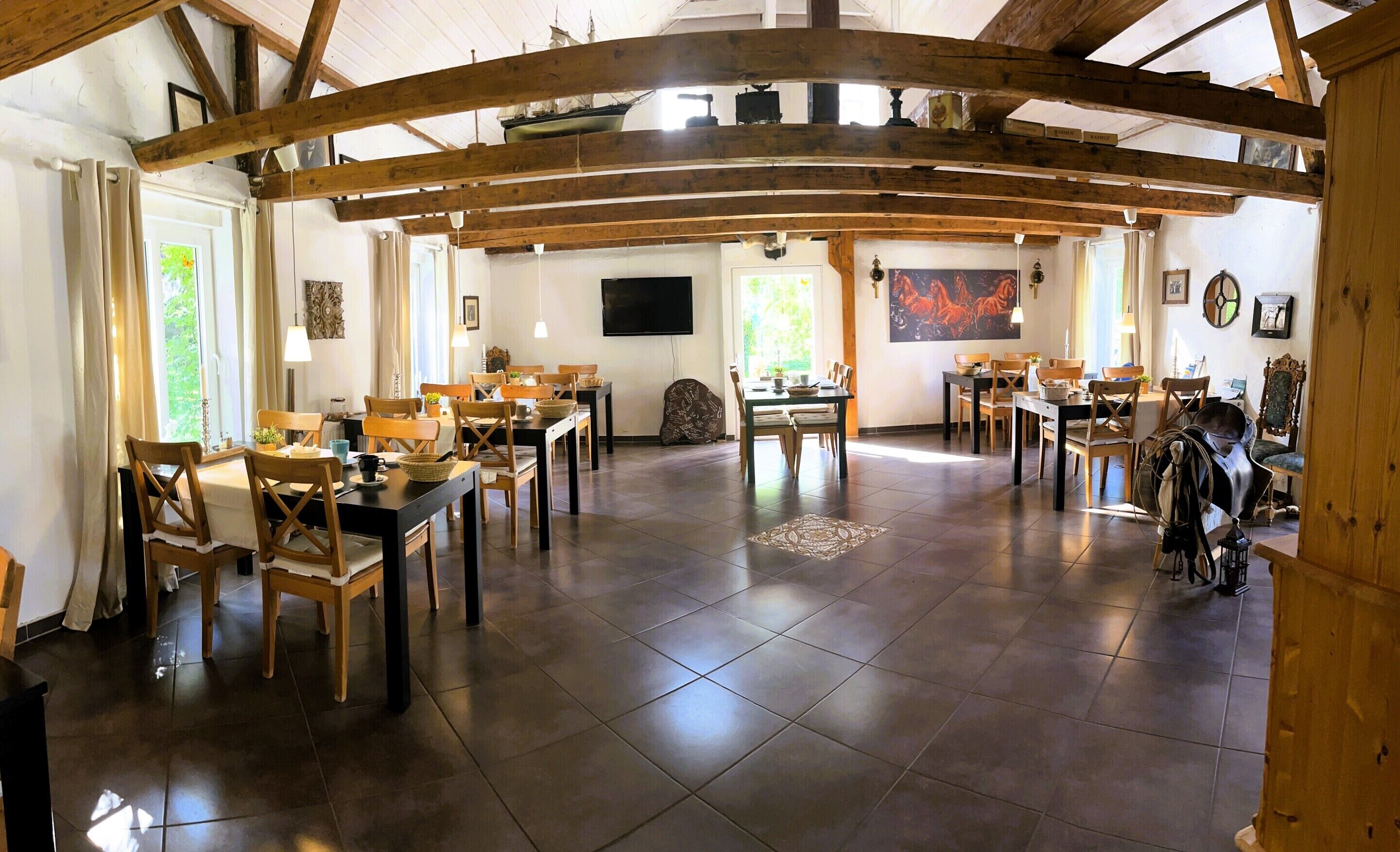 A spacious dining area with wooden beams, multiple tables, and chairs.
