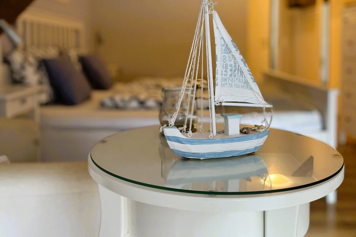Een model zeilboot op een glazen tafel in een kamer met een trap en een bank op de achtergrond.